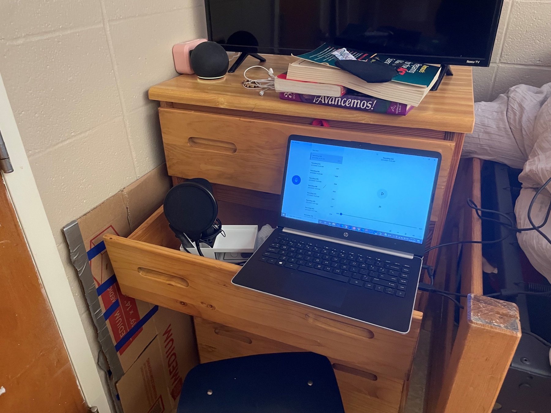 A laptop and studio microphone perched on an open drawer of a dresser to make a makeshift studio in a dorm room