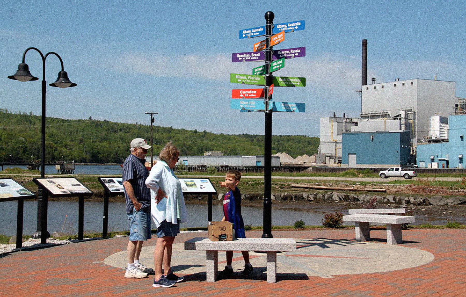 A small child points as two older adults look at him. In the background, Bucksport, Maine's paper mill can be seen.