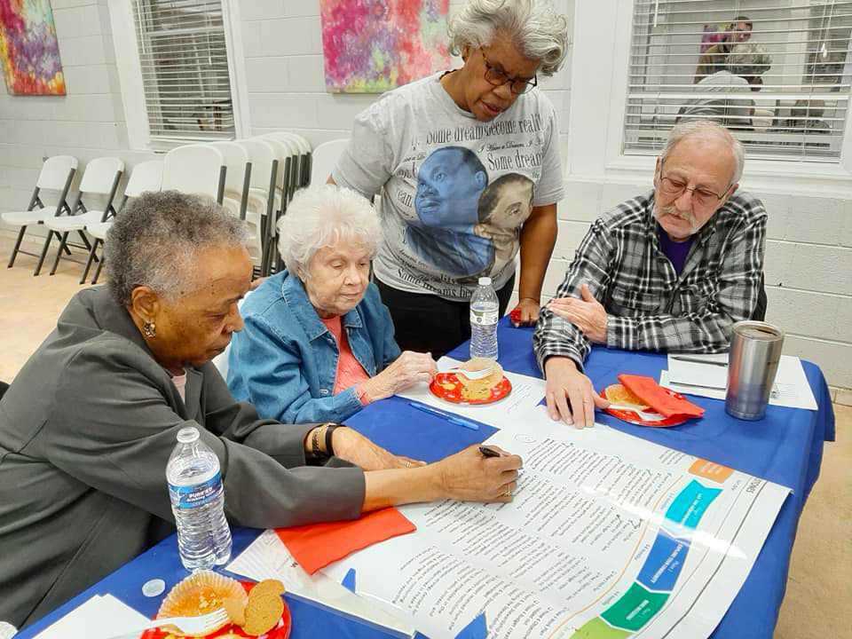 Fort Lawn community residents gather around a table and check items on a large poster board.