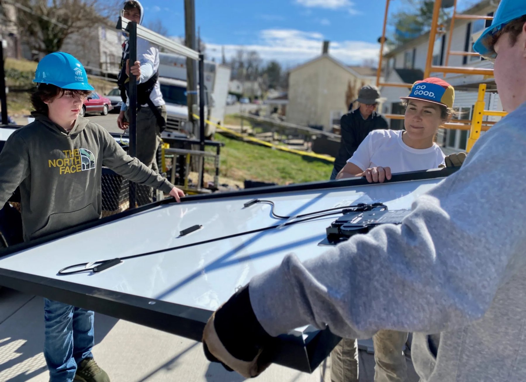 Three people lift a solar panel.