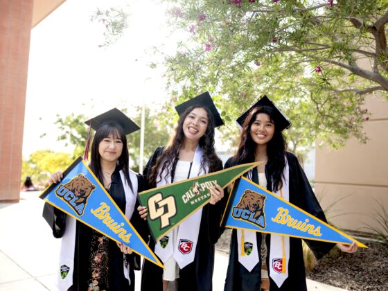 Three young high school graduates holding pennants from the universities they will attend. Two are going to UCLA, and one to Cal Poly.